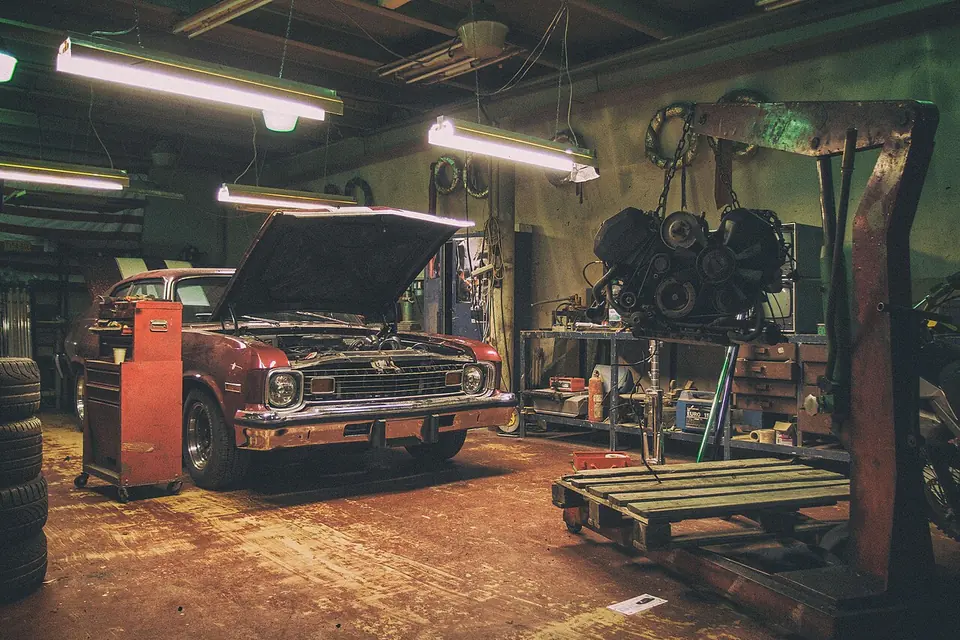 Intérieur d'un garage de réparation automobile avec une voiture ancienne et un moteur sur un établi